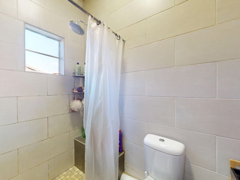 A functional bathroom featuring tiled walls and flooring, a shower area with a curtain, and a standard toilet.