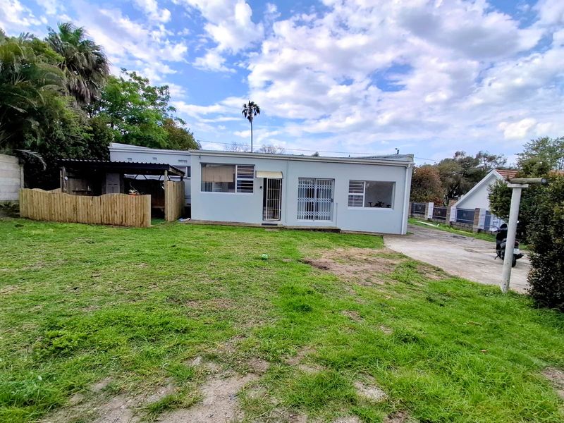 Rear view of the property featuring a lawn, concrete driveway, timber fencing, and a covered outdoor structure attached to the main building.