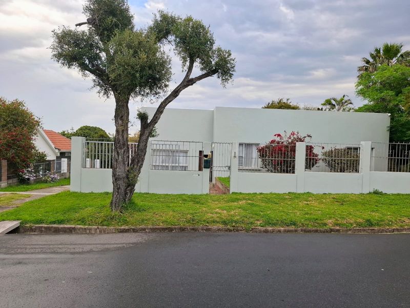 Front view of a residential property featuring a perimeter wall with metal security fencing, a gated entrance, and a paved walkway leading to the house.