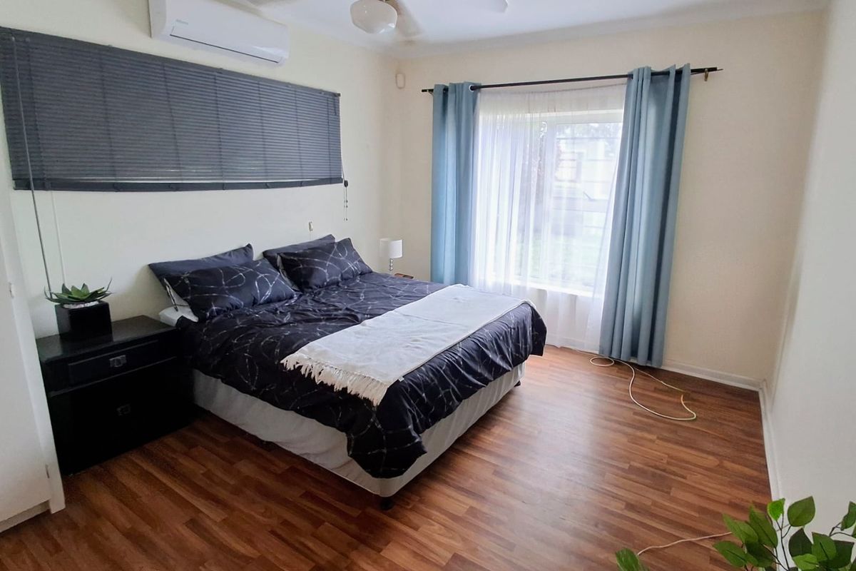 A well-lit bedroom featuring laminate flooring, a ceiling fan, and a wall-mounted split-system air conditioner.