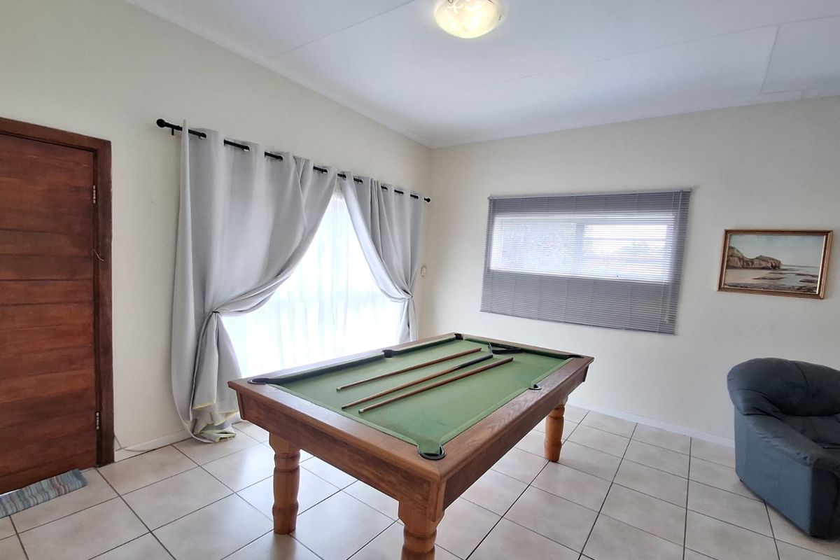 A spacious living area featuring neutral tiled flooring, natural light through window blinds, and a solid wooden door.