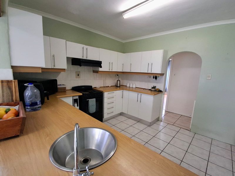Functional kitchen featuring white cabinetry, laminate countertops, a stainless steel sink, and a freestanding stove, with tiled flooring and an arched entryway.