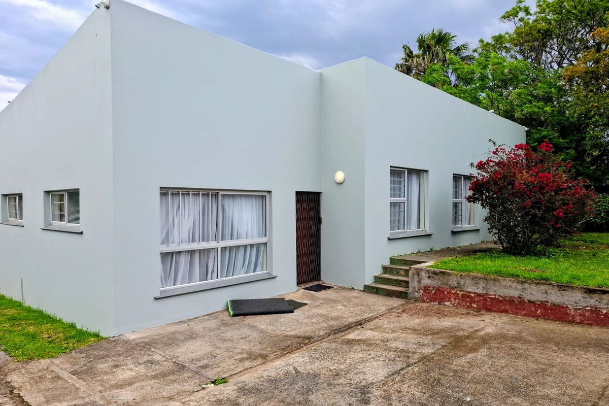 Rear exterior view of the house featuring a concrete driveway, security gate, and a raised garden area with a retaining wall.