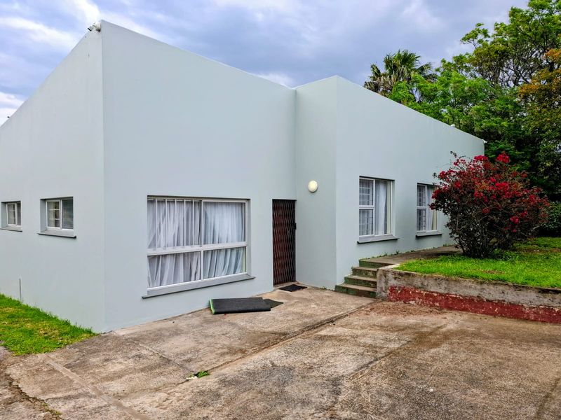 Rear exterior view of the house featuring a concrete driveway, security gate, and a raised garden area with a retaining wall.