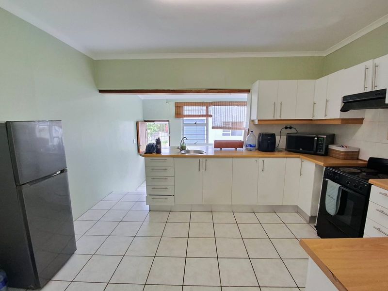 A functional kitchen featuring white cabinetry, wooden countertops, tiled flooring, and integrated appliances, offering a clean and practical workspace.