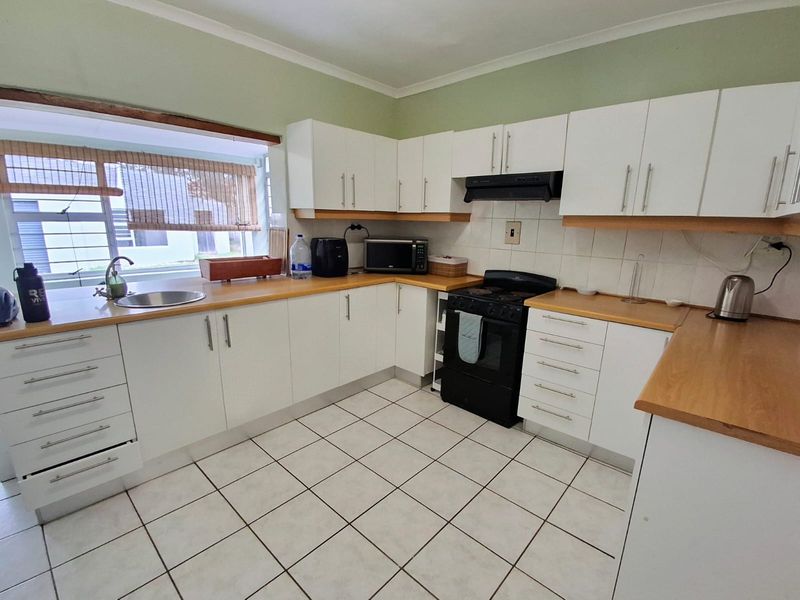 Functional kitchen featuring white cabinetry, wooden countertops, tiled flooring, and a built-in extractor fan with a freestanding stove.