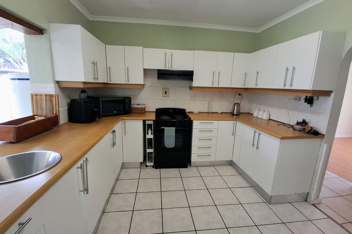 A functional kitchen featuring white cabinetry, wood-look laminate countertops, a freestanding stove with extractor fan, and tiled flooring.
