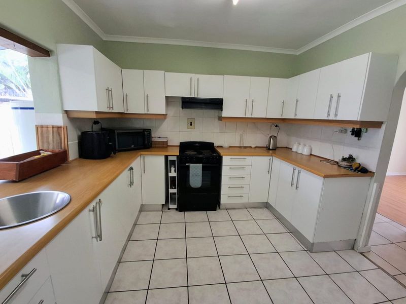 A functional kitchen featuring white cabinetry, wood-look laminate countertops, a freestanding stove with extractor fan, and tiled flooring.