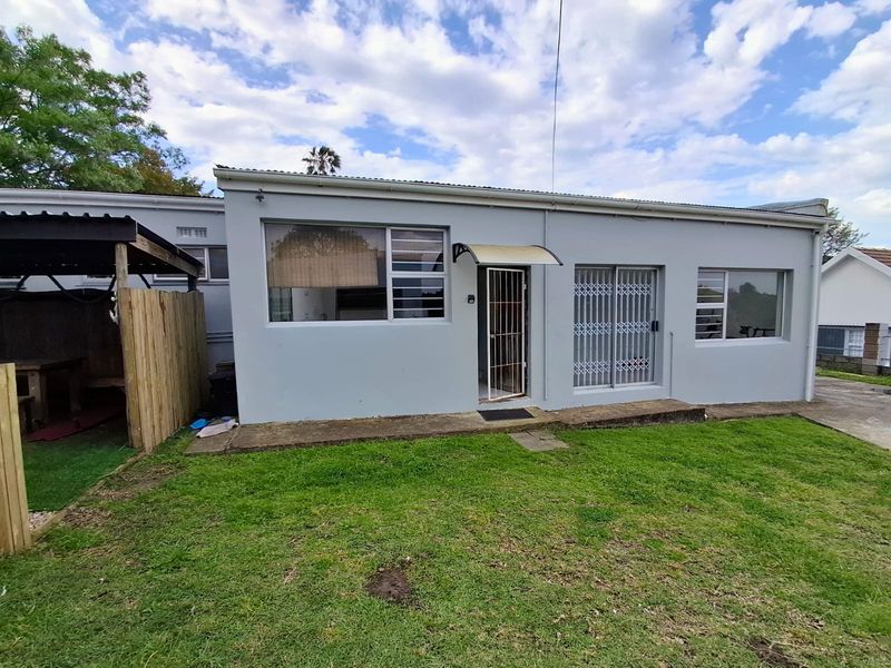 Rear view of the property featuring a concrete patio, sliding glass doors with security gates, and a small garden area.