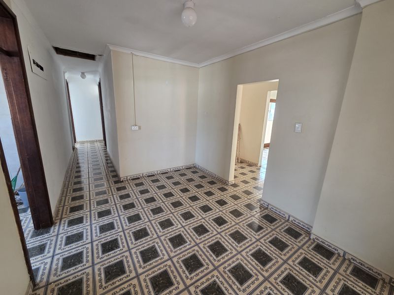 An empty hallway featuring patterned ceramic floor tiles, coving, and visible electrical infrastructure, requiring minor ceiling repairs.