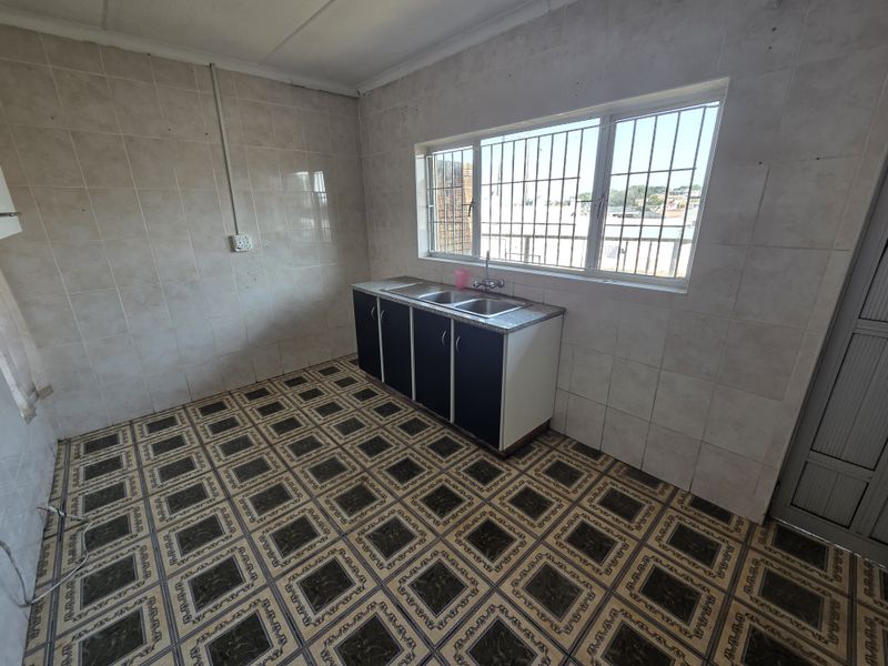 A functional, empty kitchen featuring a single sink unit, base cabinetry, tiled walls, and patterned floor tiles with security bars on the window.