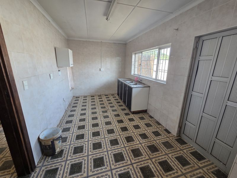 A functional, empty kitchen space featuring tiled walls, patterned floor tiles, and a basic sink unit with base cabinetry.