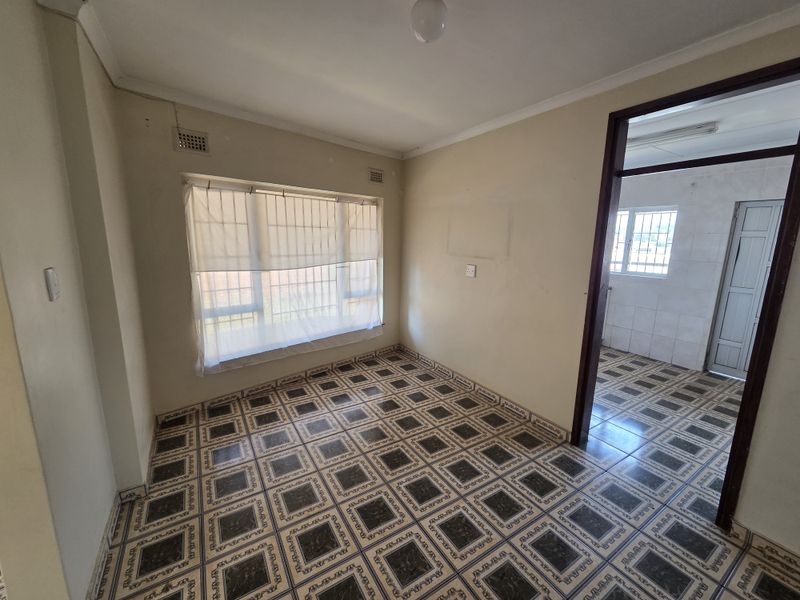 An empty bedroom featuring patterned floor tiles, cornicing, and window security bars, offering a blank canvas for renovation or restyling.