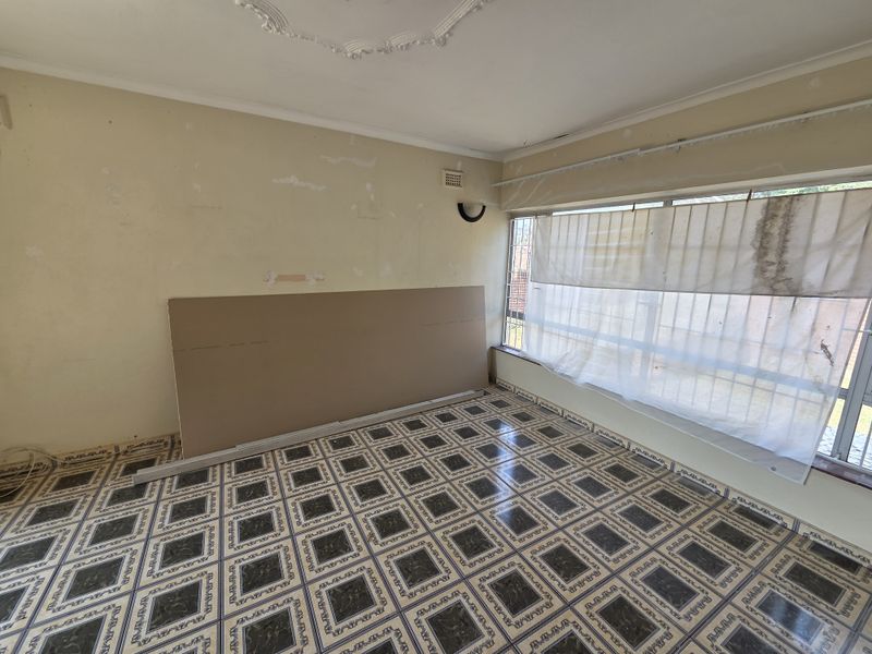 An empty bedroom featuring ornate ceiling detailing, tiled flooring, and large windows. The room requires cosmetic updates and wall repairs to restore its appeal.