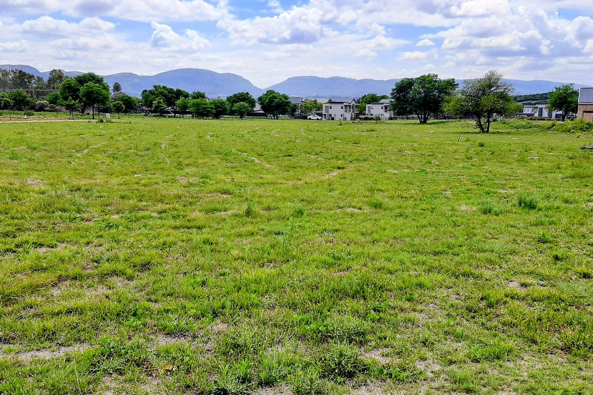 A wide, open residential vacant land plot featuring natural grass cover and distant mountain views.