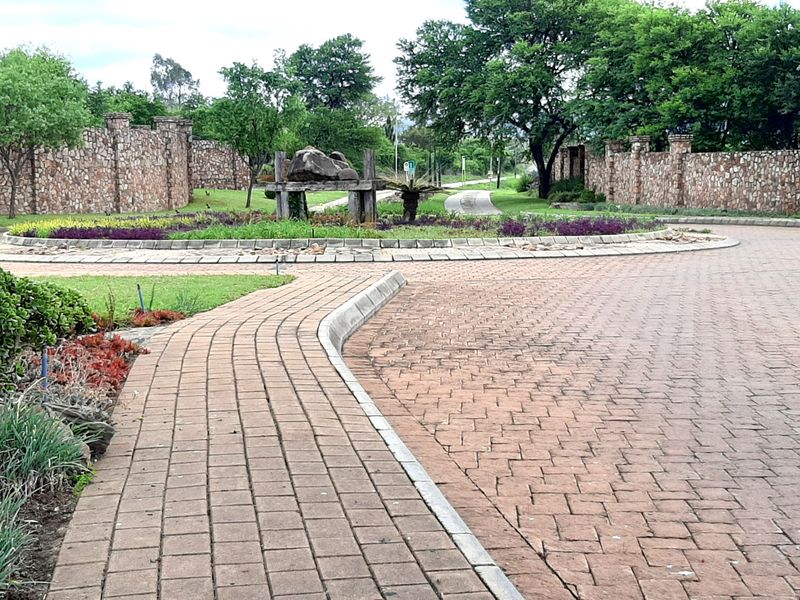 A well-maintained residential estate entrance featuring paved driveways, stone boundary walls, and landscaped garden areas.