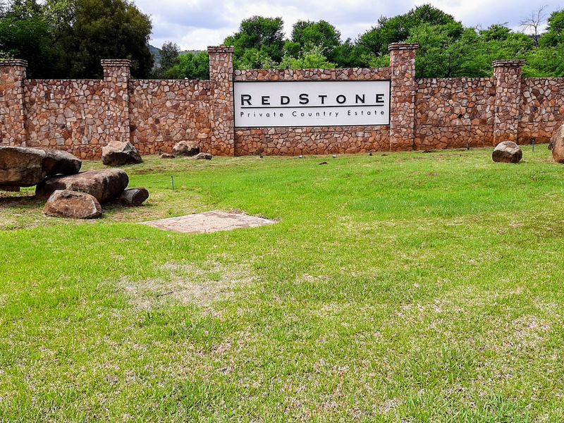 The entrance to Redstone Private Country Estate featuring a prominent stone boundary wall, estate signage, and well-maintained landscaped grounds.