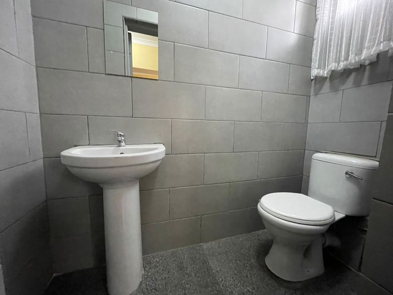 A functional bathroom featuring full-height wall tiling, a pedestal basin, and a standard toilet.