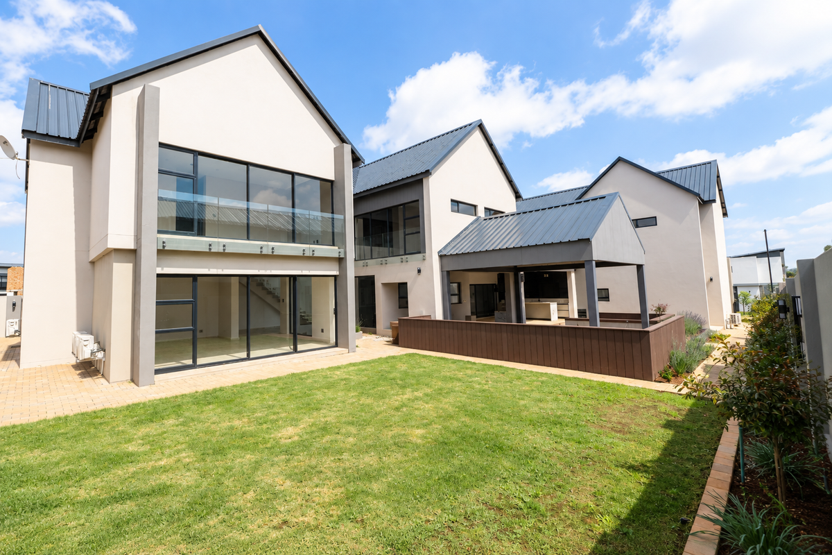 Modern rear elevation featuring a spacious lawn, paved patio, covered outdoor entertainment area, and large glass sliding doors leading to the interior.