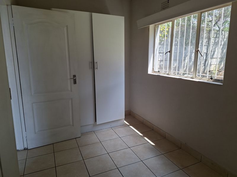 A clean, empty bedroom featuring tiled flooring, a built-in wardrobe, and a window fitted with security bars.
