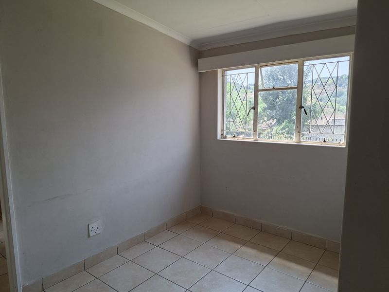 A vacant bedroom featuring neutral tiled flooring, coving, and a window fitted with security bars, offering a blank canvas for personalization.