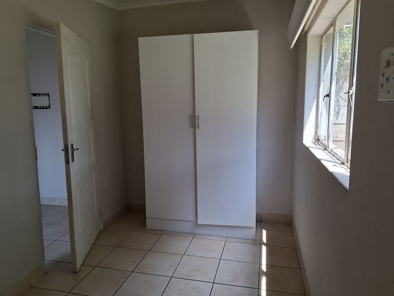 A functional bedroom featuring tiled flooring, a built-in wardrobe, and natural light from a side window.
