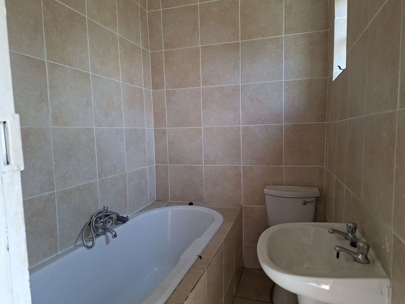 A functional bathroom featuring a built-in bathtub, pedestal basin, and toilet, finished with neutral ceramic wall tiling.