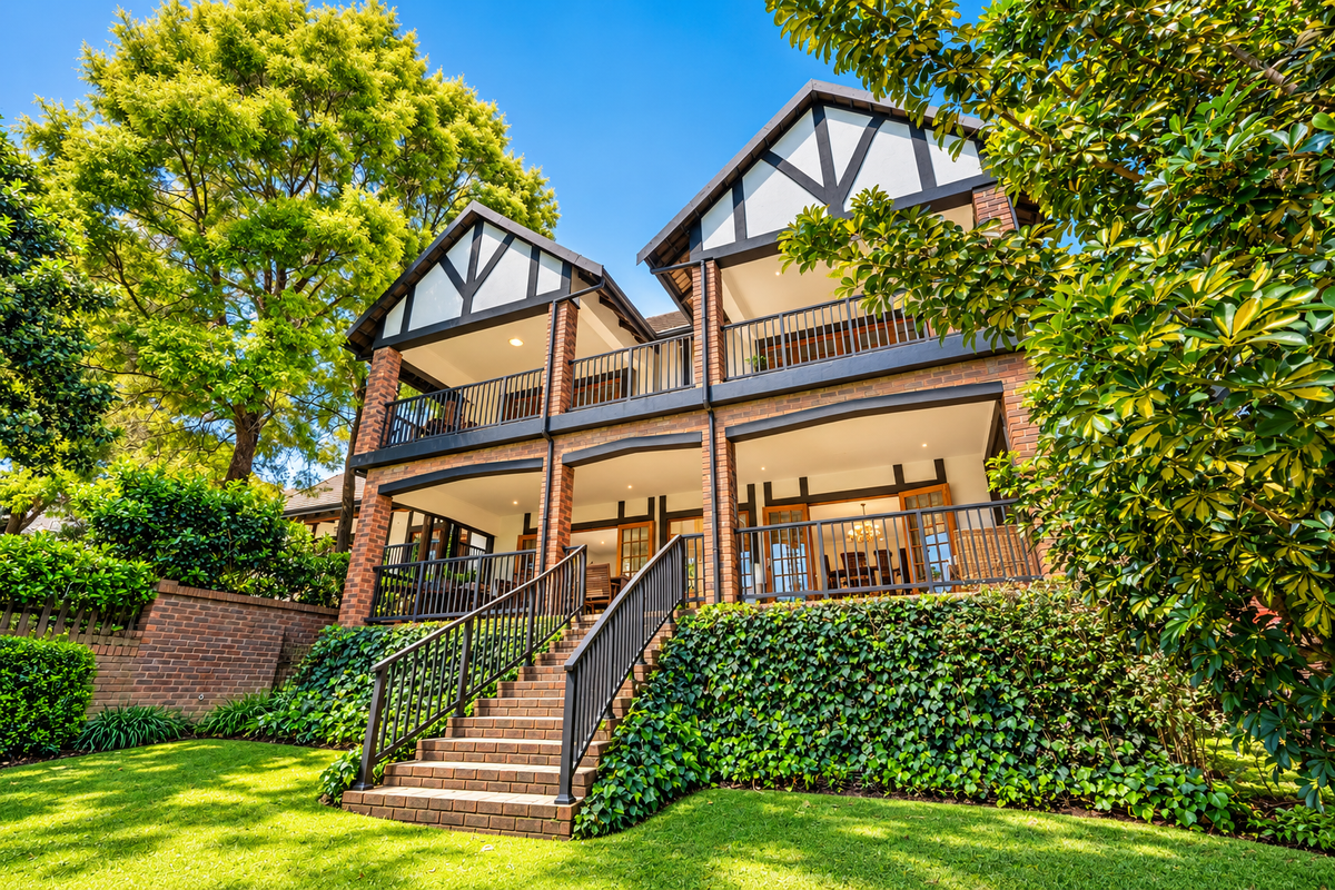 A well-maintained rear elevation of a townhouse featuring multi-level covered balconies, brick construction, and a landscaped garden with a brick staircase.