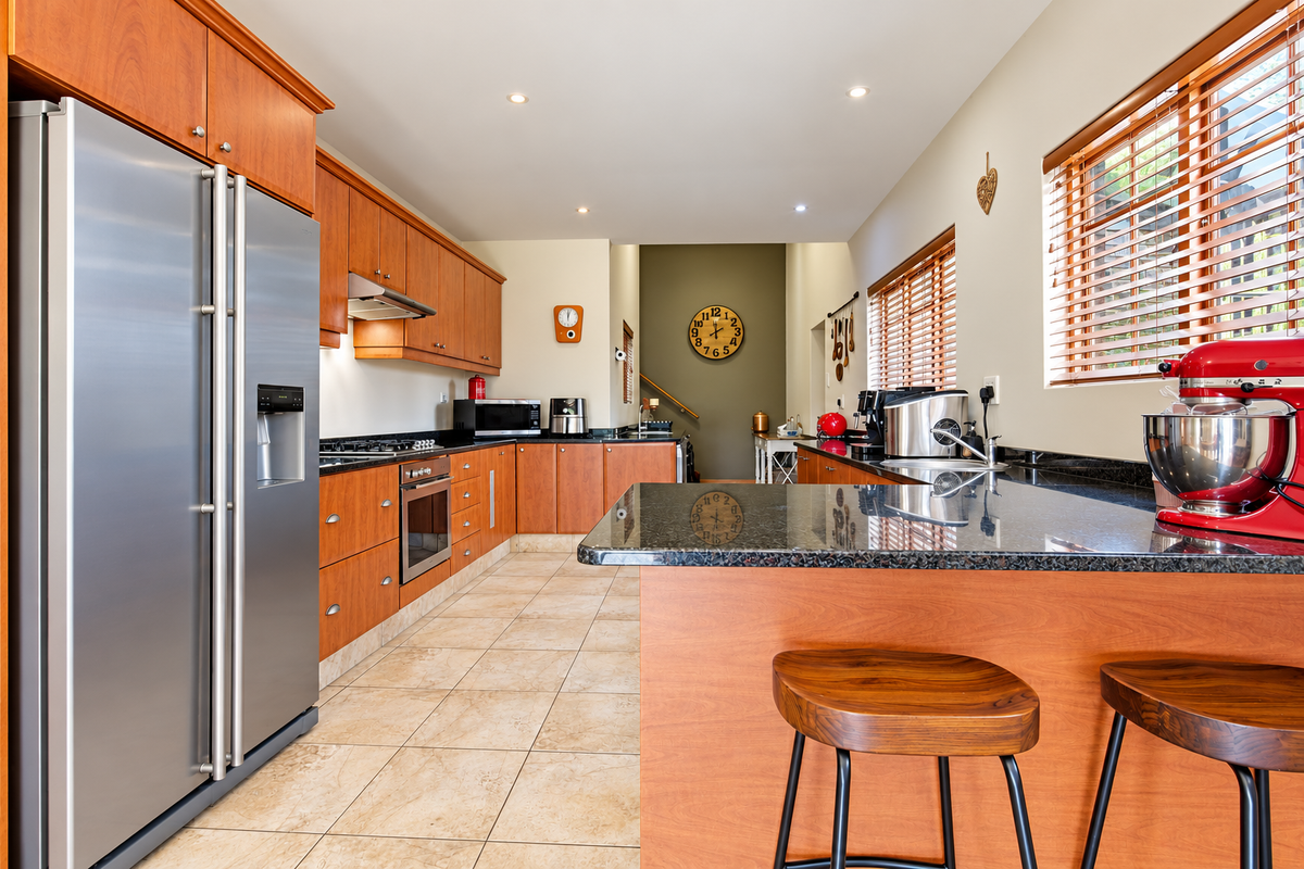 A well-maintained kitchen featuring warm wooden cabinetry, granite countertops, stainless steel appliances, and tiled flooring, offering a functional and inviting culinary space.