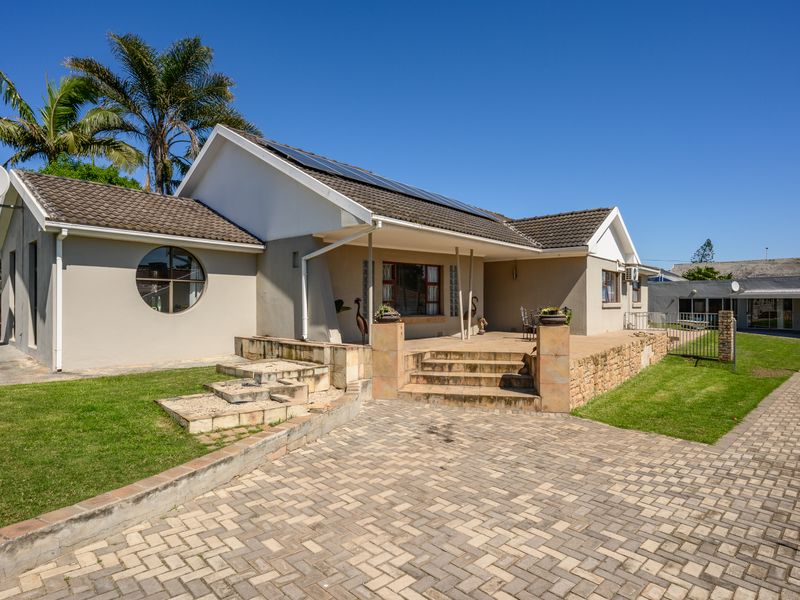 Front view of a single-story house featuring a paved driveway, raised patio area, solar panels, and distinctive circular window architecture.