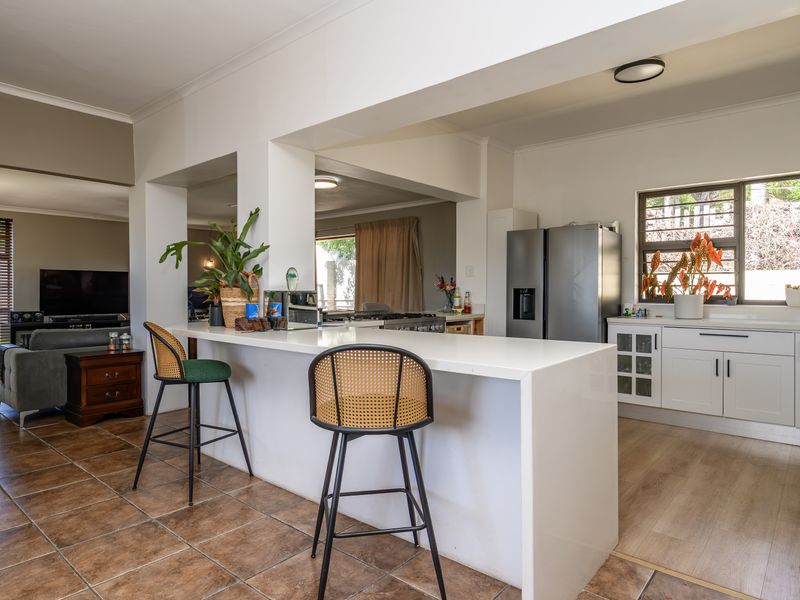 An open-plan living and kitchen area featuring a central island with a quartz countertop, white cabinetry, and a mix of tiled and laminate flooring.