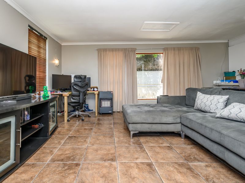 A spacious living area featuring durable tiled flooring, neutral wall tones, and natural light through large windows with curtain treatments.