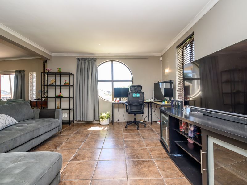 A spacious living area featuring ceramic tile flooring, a distinctive circular window, and a glass block partition, offering a versatile layout for relaxation or work.