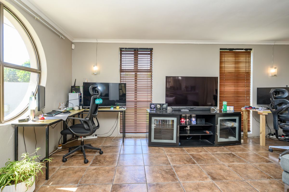 A living area featuring tiled flooring, a distinctive circular window, and venetian blinds, offering a functional space with natural light.