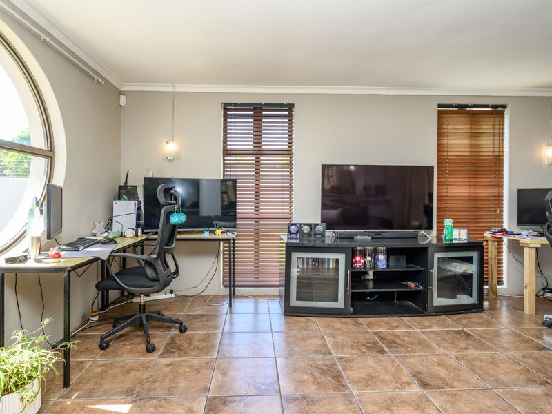 A living area featuring tiled flooring, a distinctive circular window, and venetian blinds, offering a functional space with natural light.