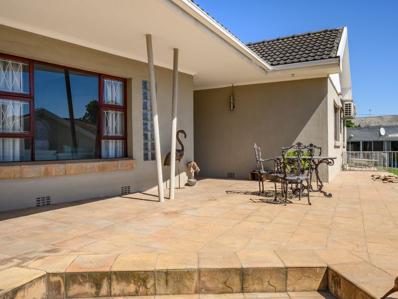 A spacious covered patio area featuring tiled flooring, a decorative glass block wall, and structural support columns, offering a functional outdoor living space.