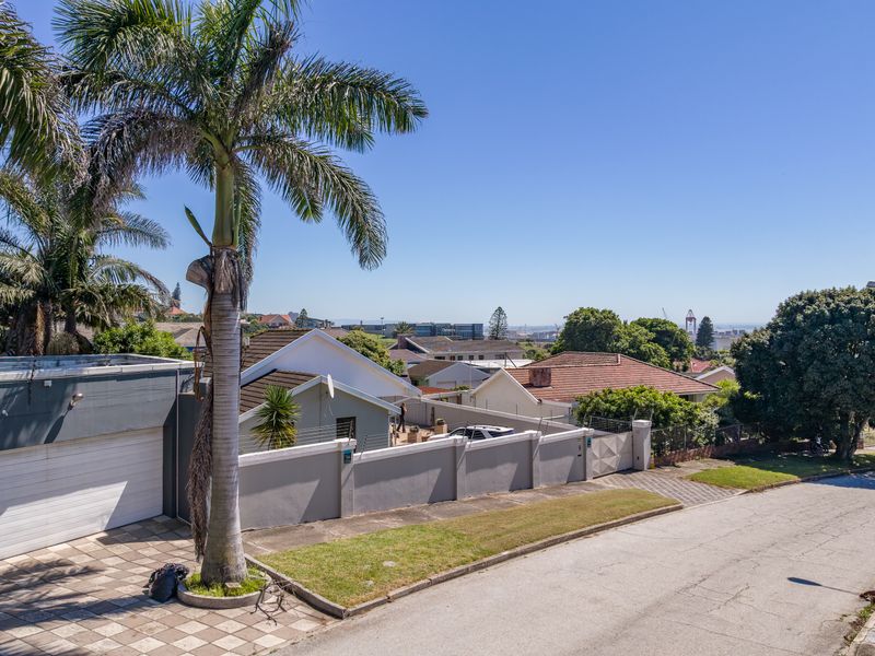 A street-level view of the property exterior, showcasing the boundary wall, electric fencing, paved driveway, and garage entrance in a residential neighborhood.