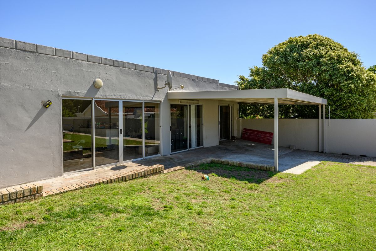 Rear view of the property featuring a covered patio area, sliding glass doors, and a paved outdoor space leading to the garden.