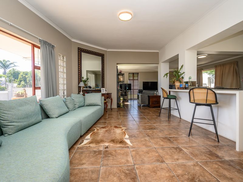 Spacious open-plan living area featuring tiled flooring, a breakfast bar, and a glass block feature wall, seamlessly connecting to the kitchen and patio.