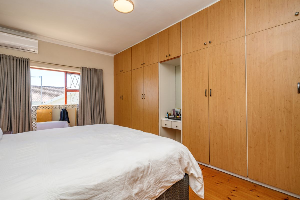 A well-maintained bedroom featuring extensive floor-to-ceiling built-in wooden cupboards with an integrated vanity area, timber flooring, and a wall-mounted air conditioning unit.