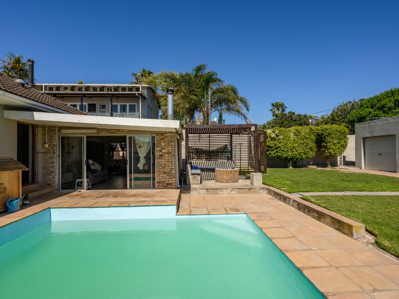 Outdoor entertainment area featuring a swimming pool, tiled deck, covered patio with timber pergola, and a spacious lawn with a detached garage.