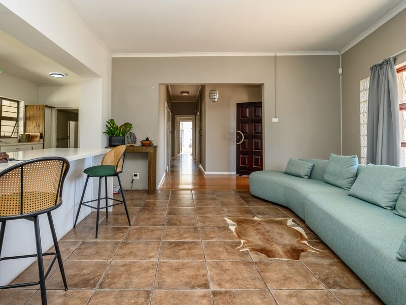 An open-plan living area featuring tiled floors, a breakfast bar connecting to the kitchen, and a hallway leading to the main entrance.