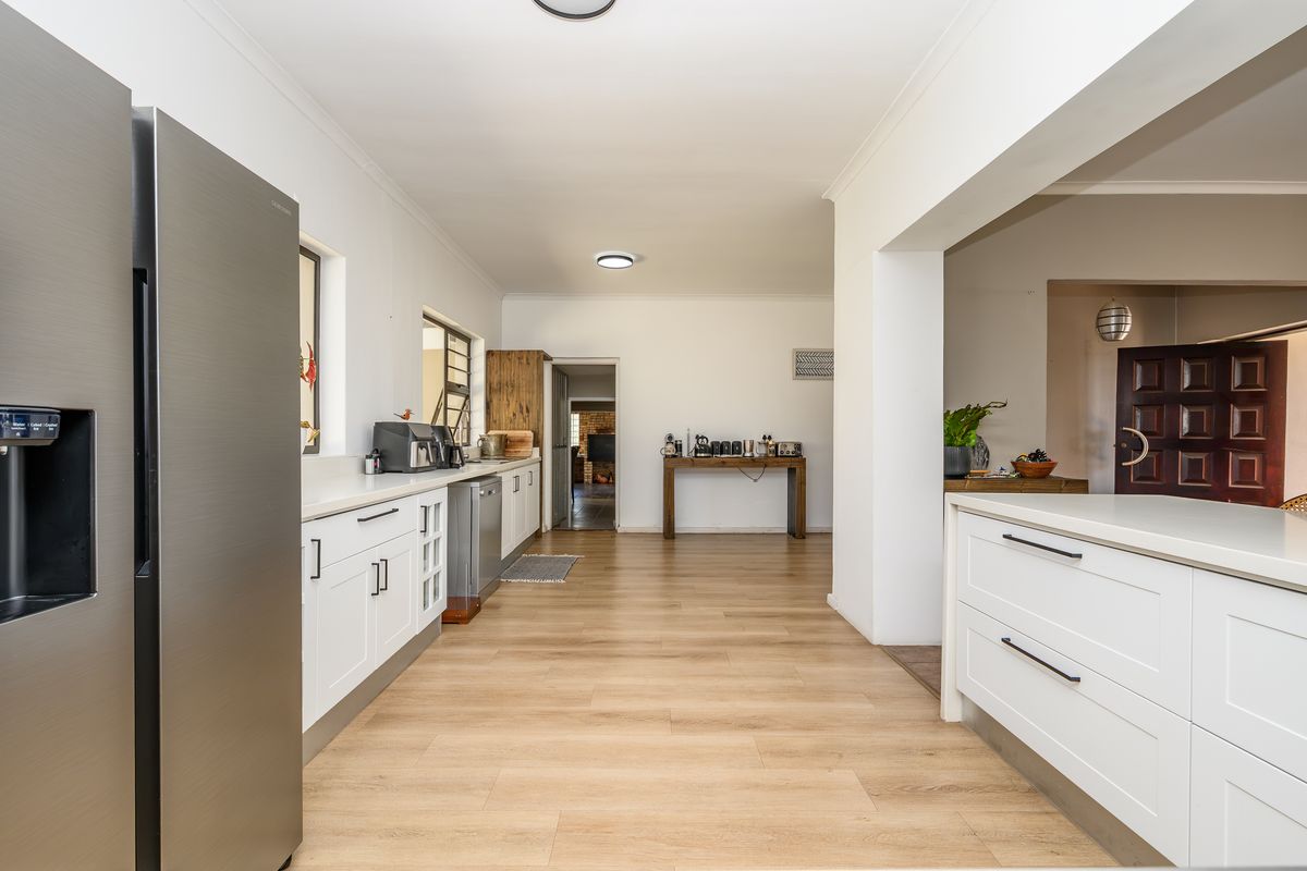 Modern kitchen featuring white cabinetry, stone countertops, laminate flooring, and integrated appliances, flowing into an open-plan living area.