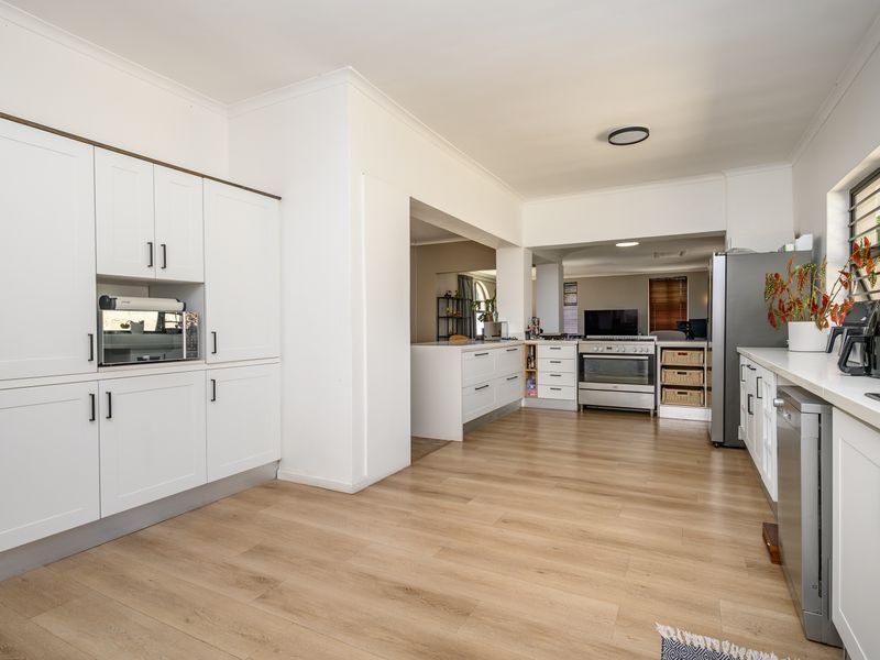 A bright, modern kitchen featuring white cabinetry, wood-look laminate flooring, and integrated stainless steel appliances, offering a clean and functional layout.