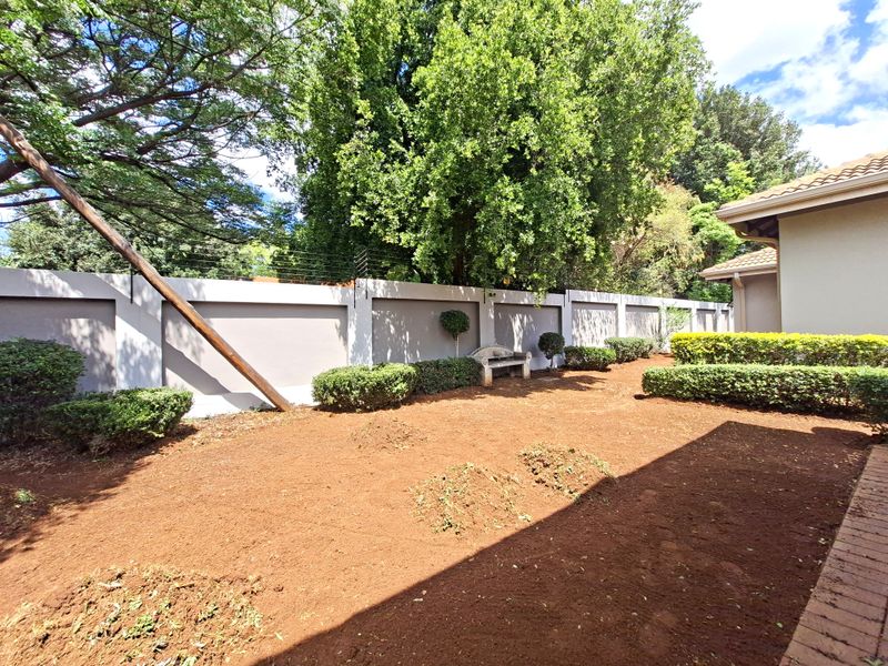 A private rear garden featuring a perimeter wall with electric fencing and established landscaping, currently awaiting lawn installation or further garden development.