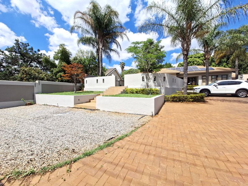 Front exterior view featuring a paved driveway, gravel landscaping, tiered retaining walls with concrete steps, and solar panels installed on the roof.