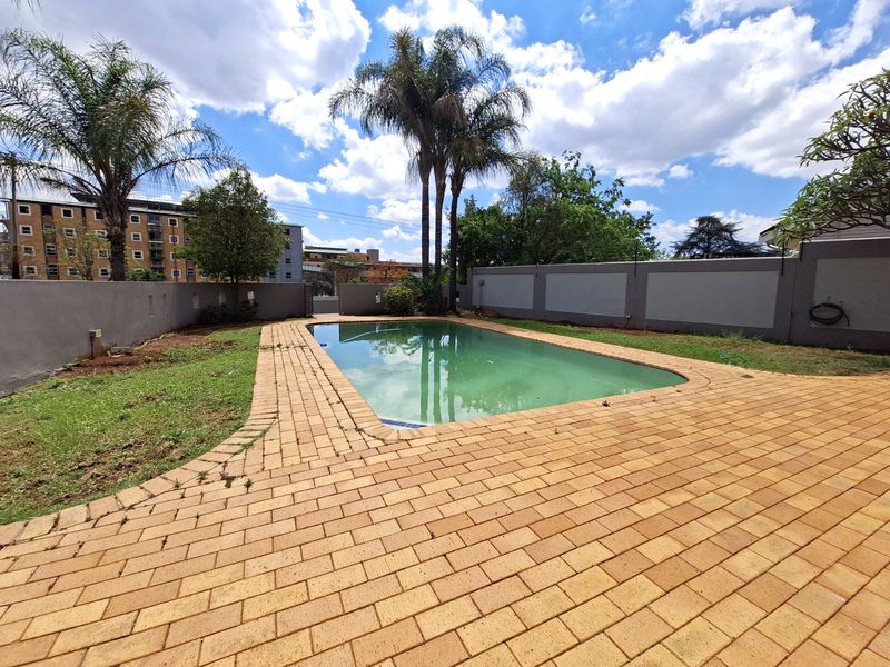 Outdoor pool area featuring a paved surround, perimeter boundary walls with electric fencing, and established palm trees in a private garden setting.