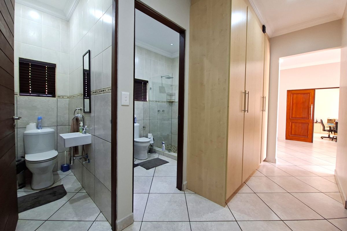 A well-maintained bathroom featuring tiled flooring, a wall-mounted basin, a glass shower enclosure, and ample built-in cupboard storage.