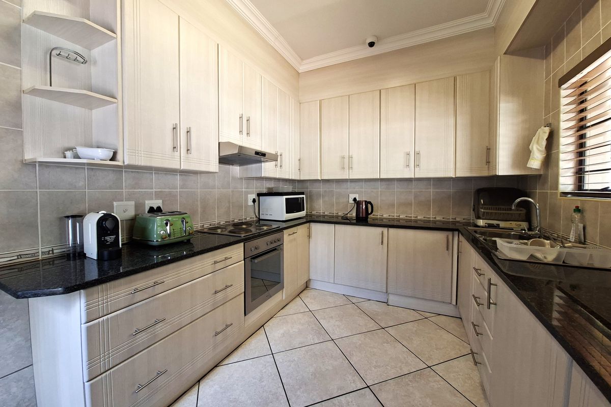 A well-maintained kitchen featuring light-toned cabinetry, granite countertops, integrated appliances, and tiled flooring with a classic backsplash.