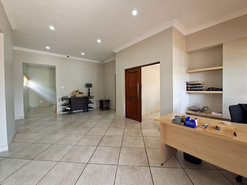 A spacious home office featuring neutral tiled flooring, recessed downlighting, crown molding, and built-in shelving units.